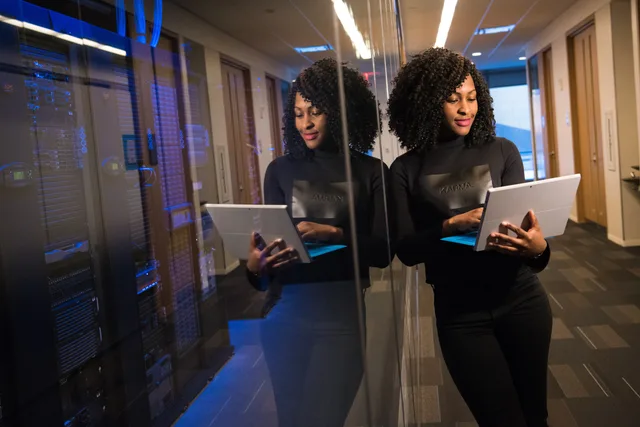 African American woman standing in modern office using laptop, reflecting professionalism and technology engagement. Customer data platform vs warehouse: which to choose?
