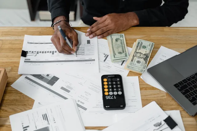 Man working on financial reports with calculator, money, and laptop on a desk. Customer data platform costs: a whole-life budget template with a worked £82,500 example